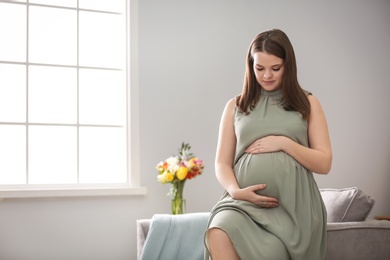 Beautiful pregnant woman sitting on armchair at home