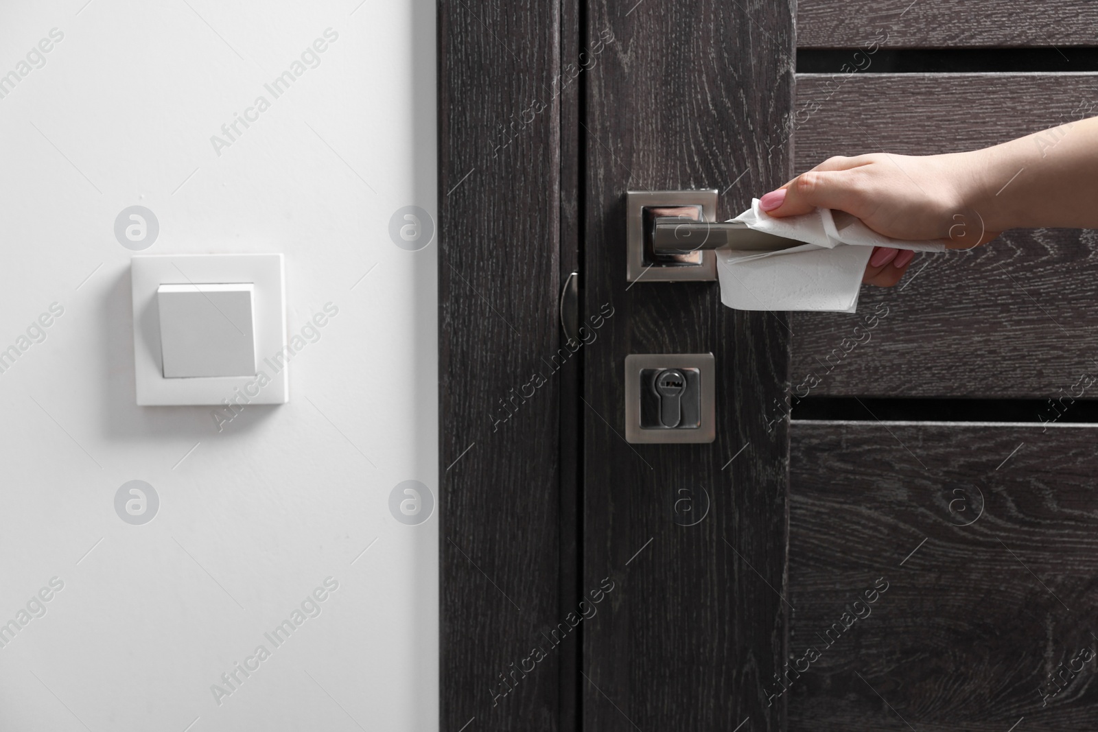 Photo of Woman wiping door handle with paper towel indoors, closeup