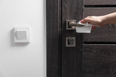 Photo of Woman wiping door handle with paper towel indoors, closeup