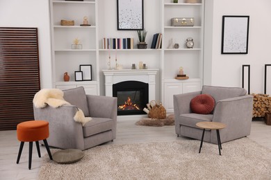 Comfortable armchairs, fireplace and shelves in living room. Interior design