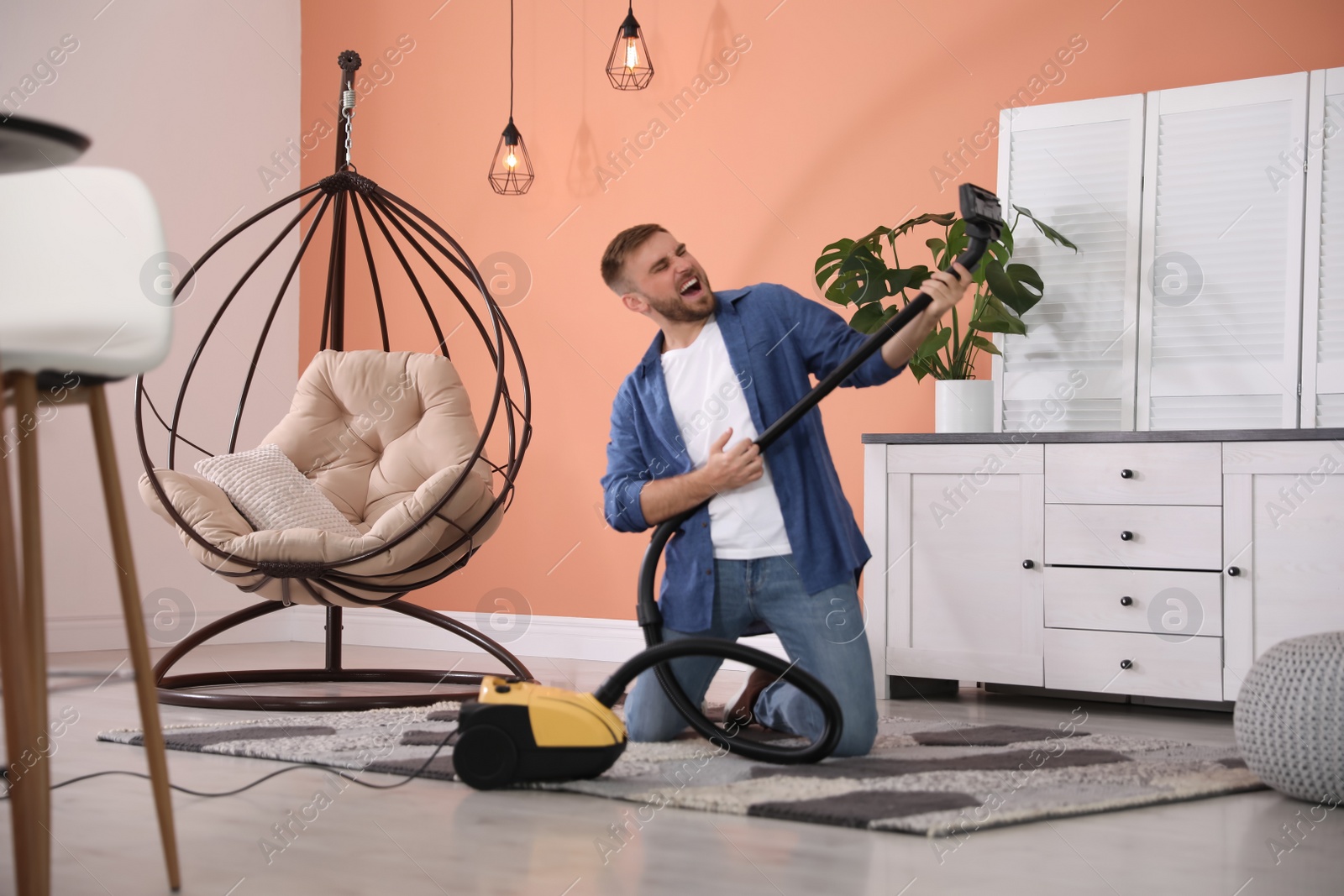 Photo of Young man having fun while vacuuming at home