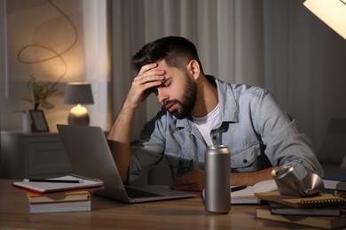 Photo of Tired young man with energy drink studying at home