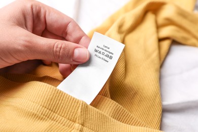 Woman holding clothing label on yellow garment, closeup