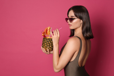Photo of Beautiful young woman with exotic cocktail wearing swimsuit and sunglasses on pink background