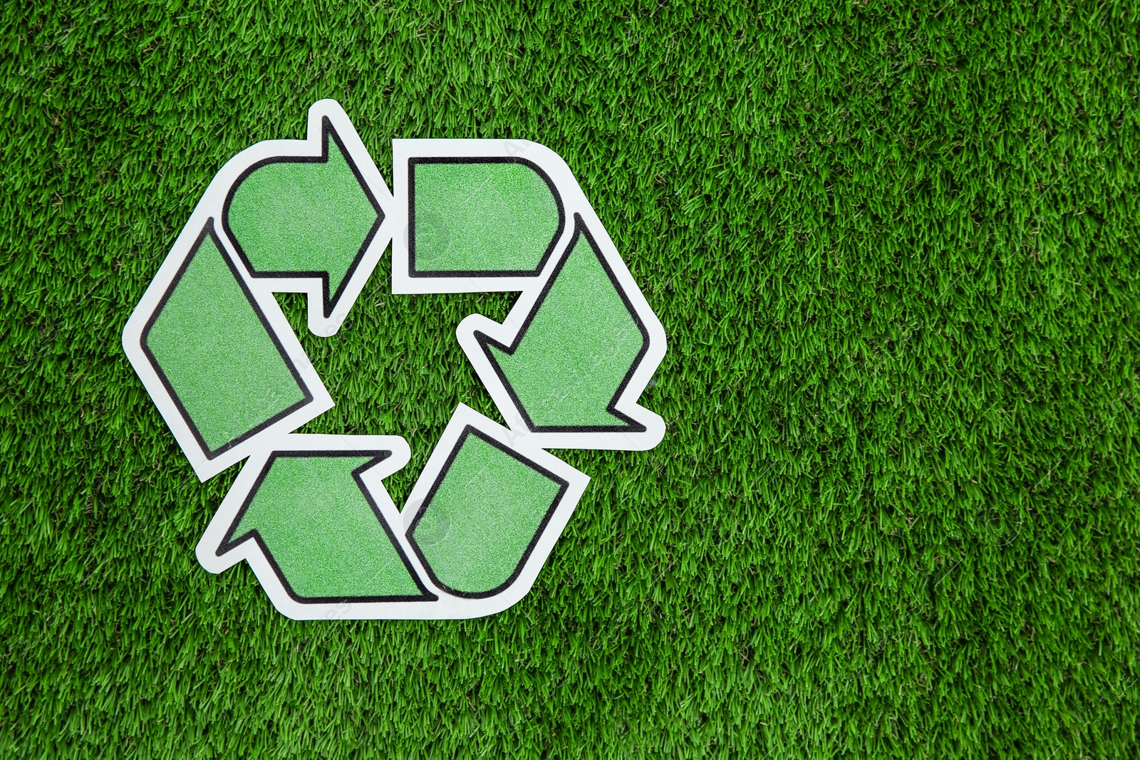 Photo of Paper recycling symbol on green grass, top view. Space for text