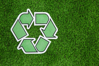 Photo of Paper recycling symbol on green grass, top view. Space for text