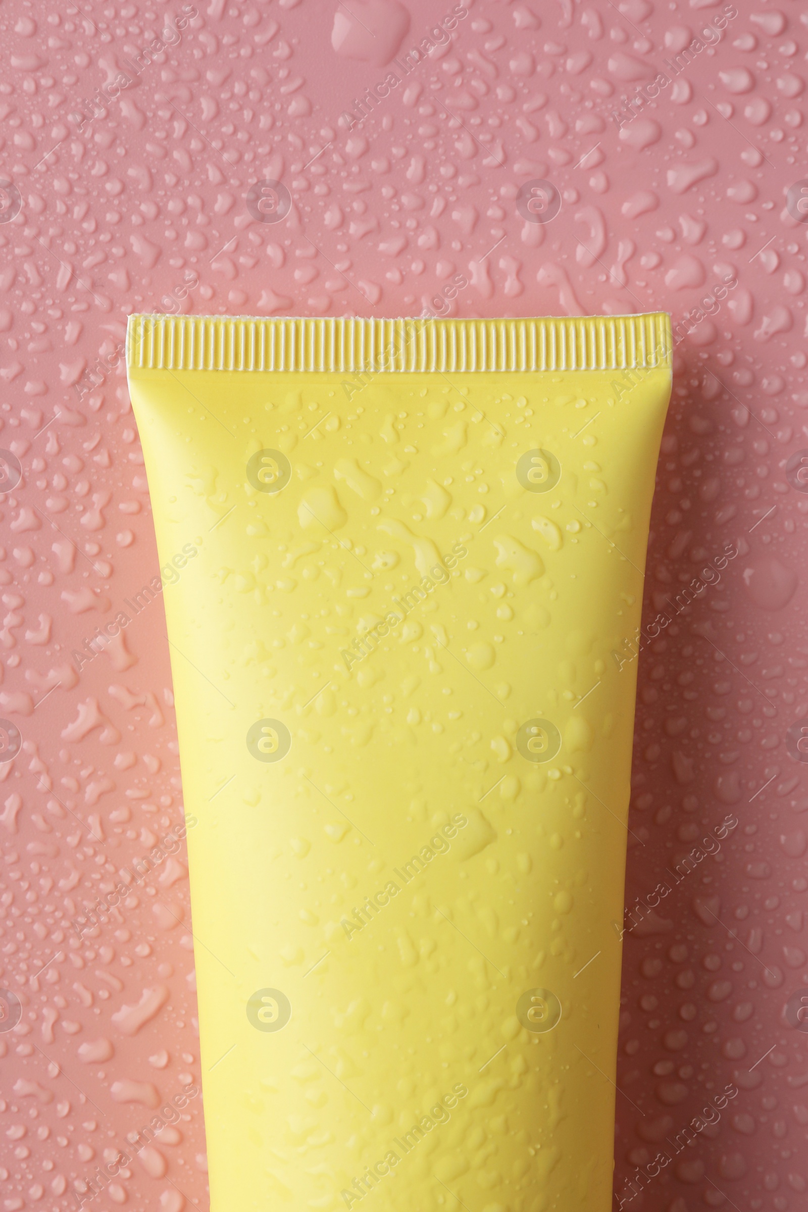 Photo of Moisturizing cream in tube on pink background with water drops, top view