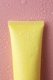 Photo of Moisturizing cream in tube on pink background with water drops, top view