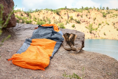Photo of Sleeping bag and boots on cliff near lake. Space for text