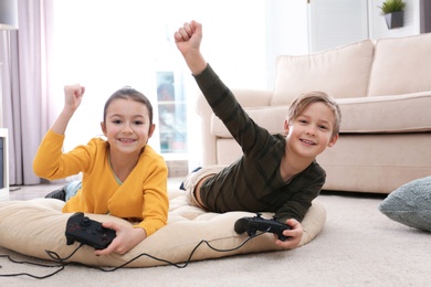 Photo of Cute children playing video games on floor at home