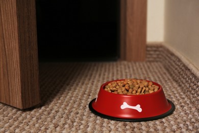 Photo of Dry dog food in feeding bowl on soft carpet indoors. Space for text