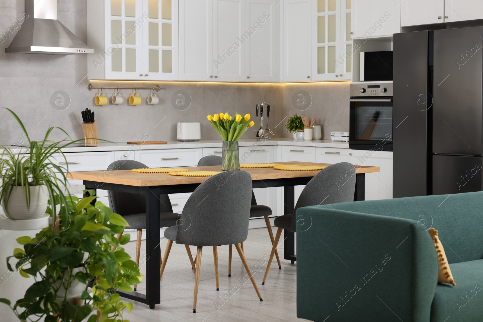 Photo of Spring atmosphere. Stylish kitchen interior with comfortable furniture and bouquet of beautiful yellow tulips