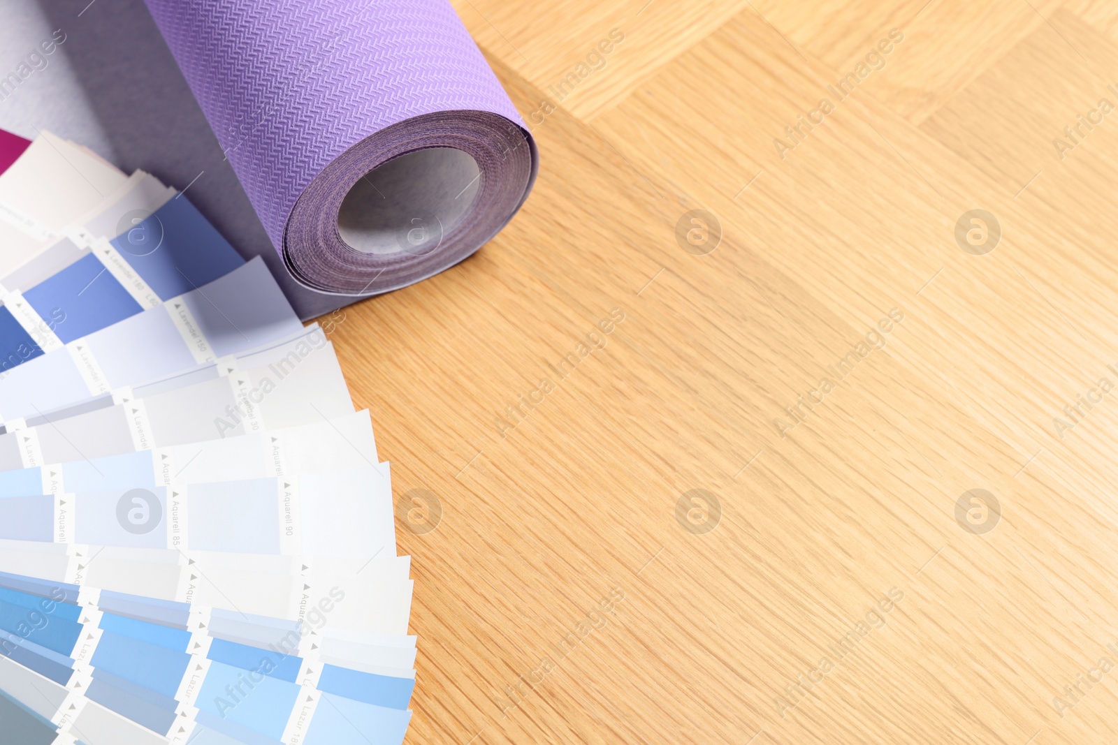 Photo of Violet wallpaper roll and color palette samples on wooden table, space for text