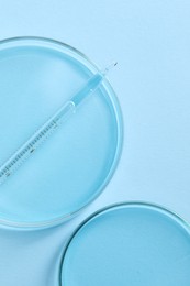 Photo of Transfer pipette and petri dishes on light blue background, flat lay