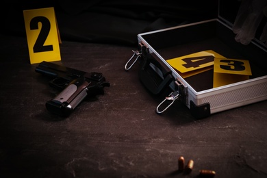 Photo of Gun and open case with evidence markers on black slate table. Crime scene