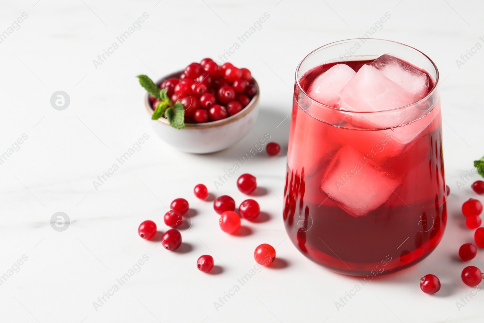 Photo of Tasty cranberry juice with ice cubes in glass and fresh berries on white wooden table, closeup. Space for text