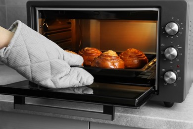 Woman taking out baking pan with delicious spiral buns from electric oven, closeup