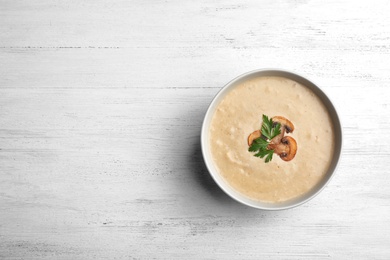 Bowl of fresh homemade mushroom soup on wooden background, top view with space for text