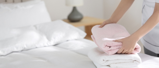 Image of Young chambermaid putting stack of fresh towels on bed in hotel room, closeup view with space for text. Banner design