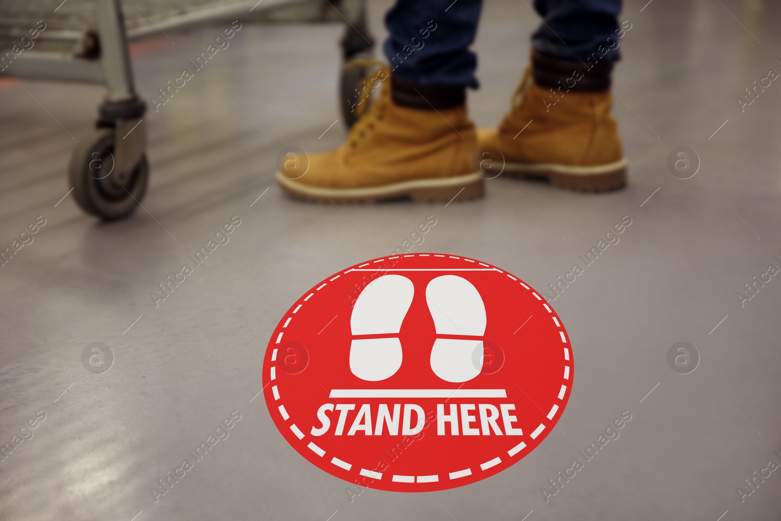 Image of Keep social distance as preventive measure during coronavirus outbreak. Red warning sign on floor near buyer with shopping cart, closeup