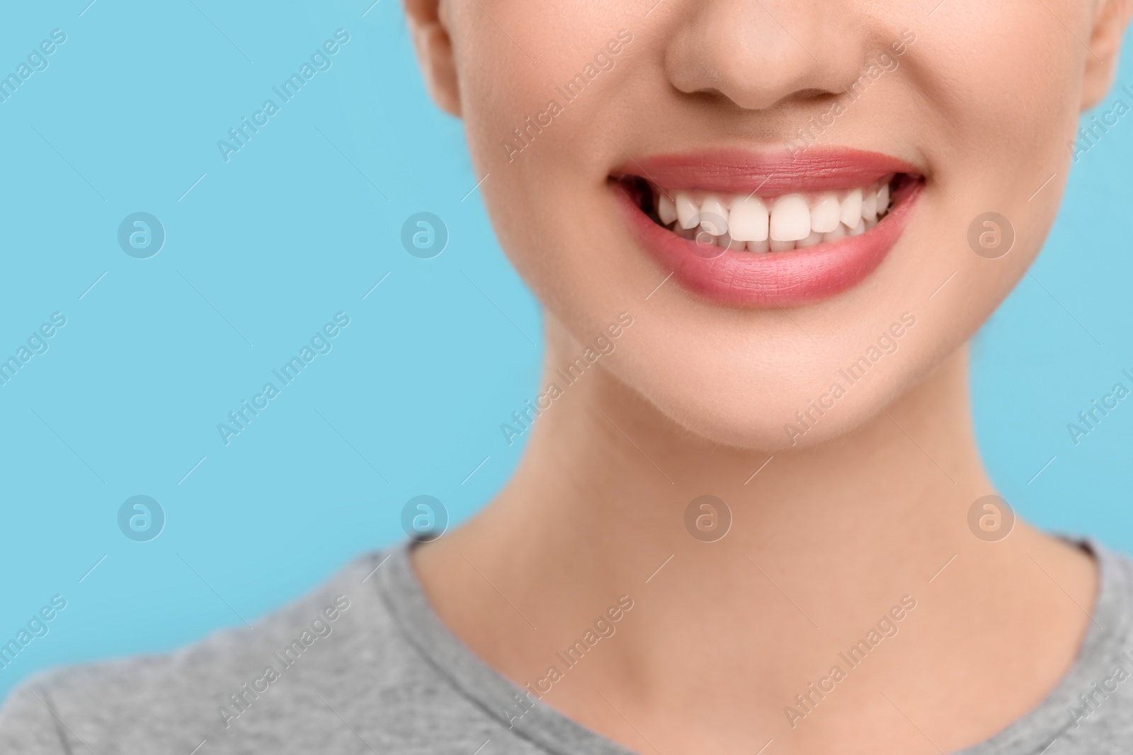 Photo of Woman with clean teeth smiling on light blue background, closeup. Space for text