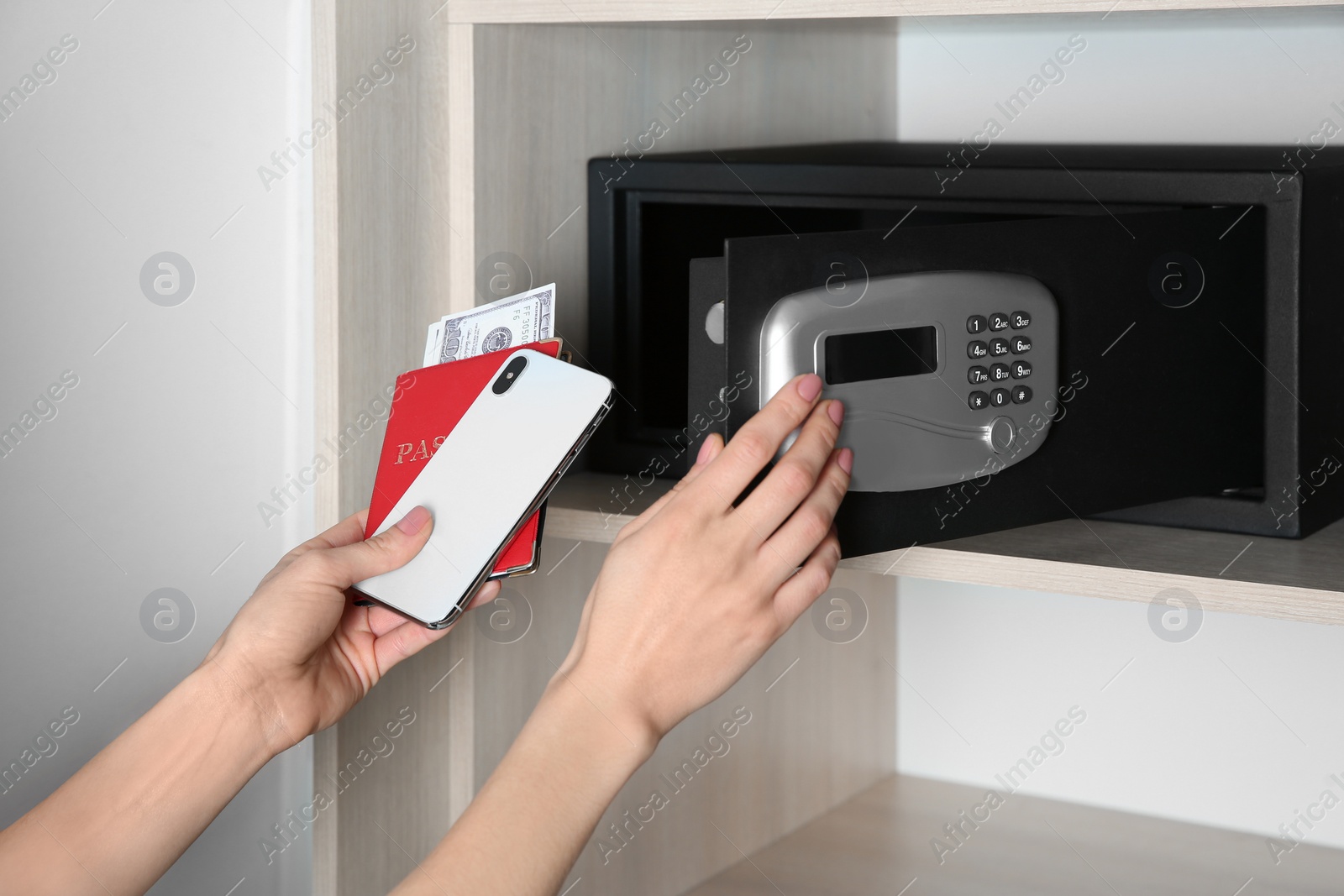 Photo of Woman putting smartphone, passport and money into steel safe, closeup