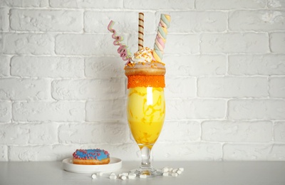 Glass of tasty milk shake with sweets on table near brick wall