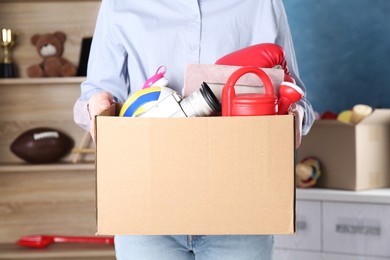Photo of Woman holding box of unwanted stuff indoors, closeup
