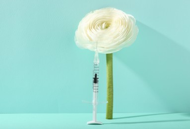 Cosmetology. Medical syringe and ranunculus flower on turquoise background