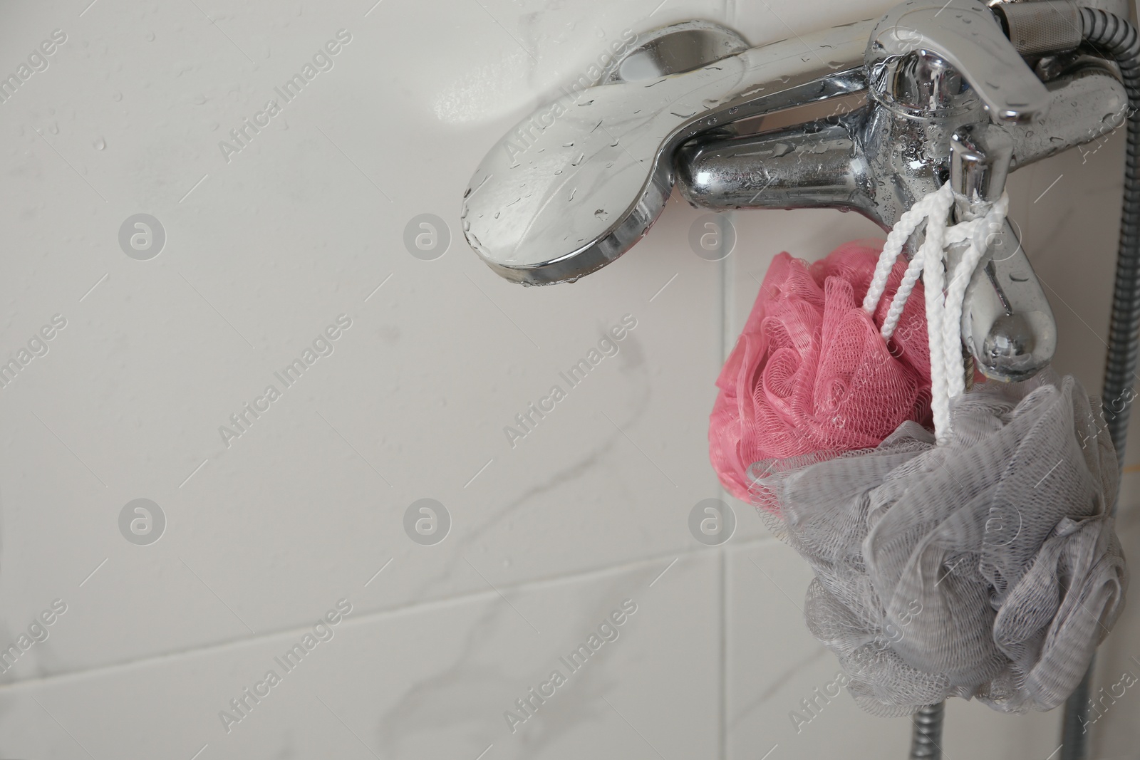 Photo of Colorful shower puffs hanging on faucet in bathroom, space for text