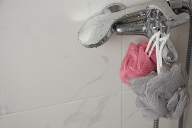 Photo of Colorful shower puffs hanging on faucet in bathroom, space for text