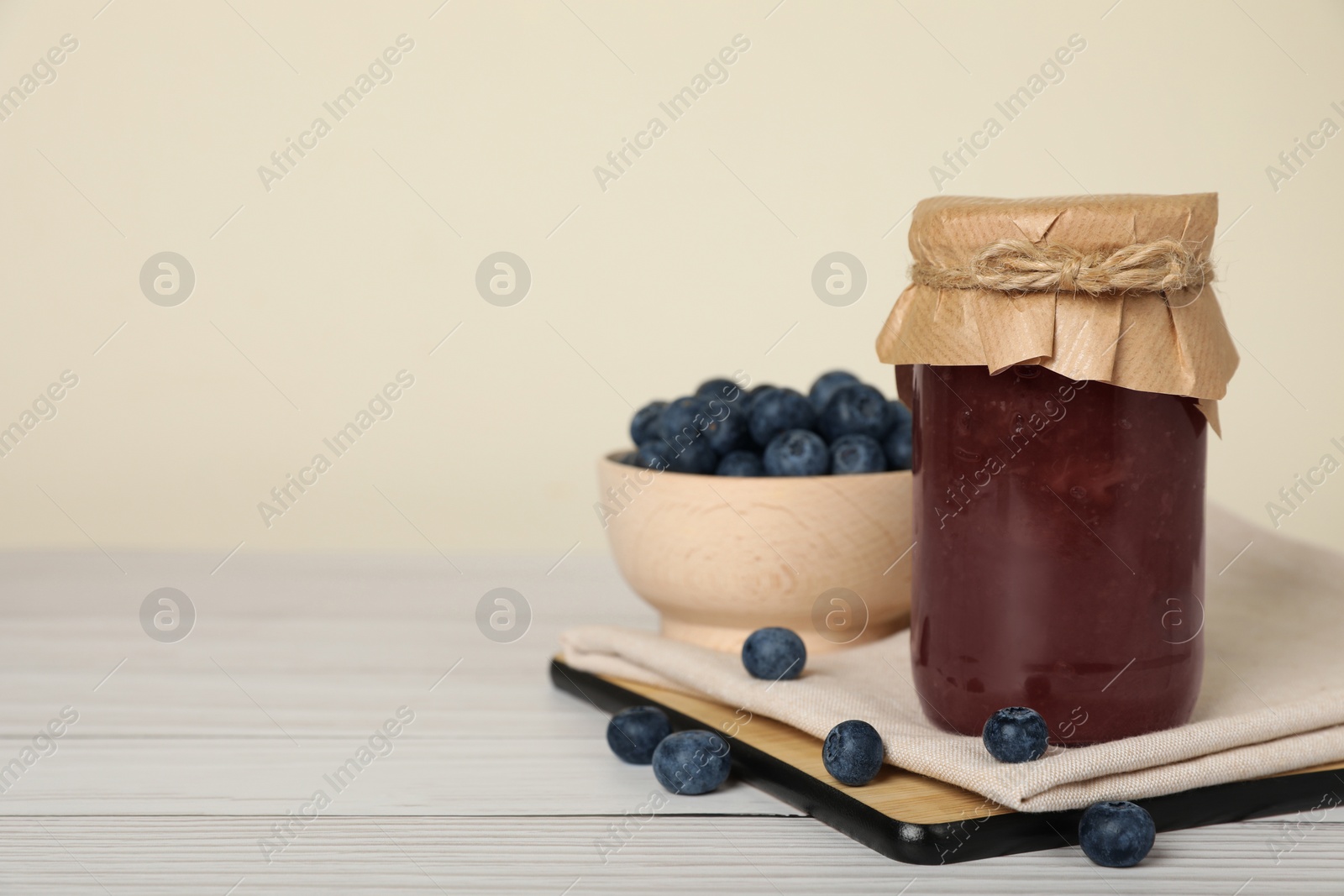 Photo of Jar of delicious canned blueberry jam and fresh berries on white wooden table. Space for text