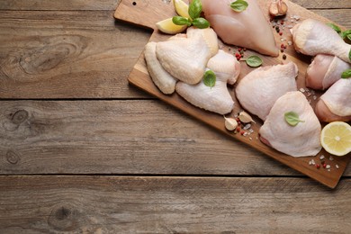 Photo of Board with fresh raw chicken wings and other products on wooden table, top view. Space for text
