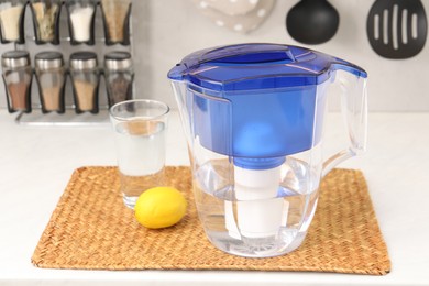 Photo of Water filter jug, glass and lemon on white countertop in kitchen