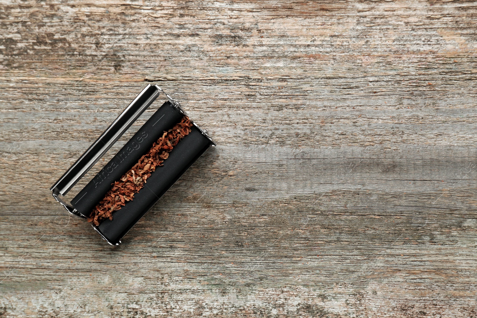 Photo of Roller with tobacco on old wooden table, top view. Making hand rolled cigarettes