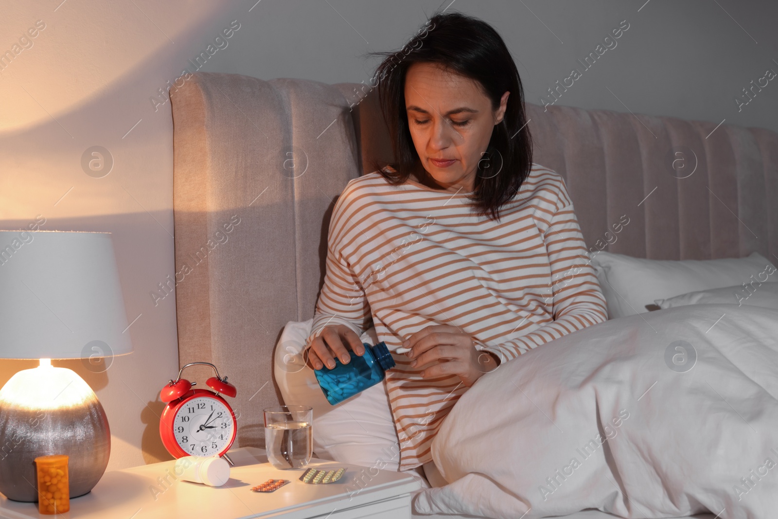 Photo of Mature woman with bottle of pills suffering from insomnia in bed at night