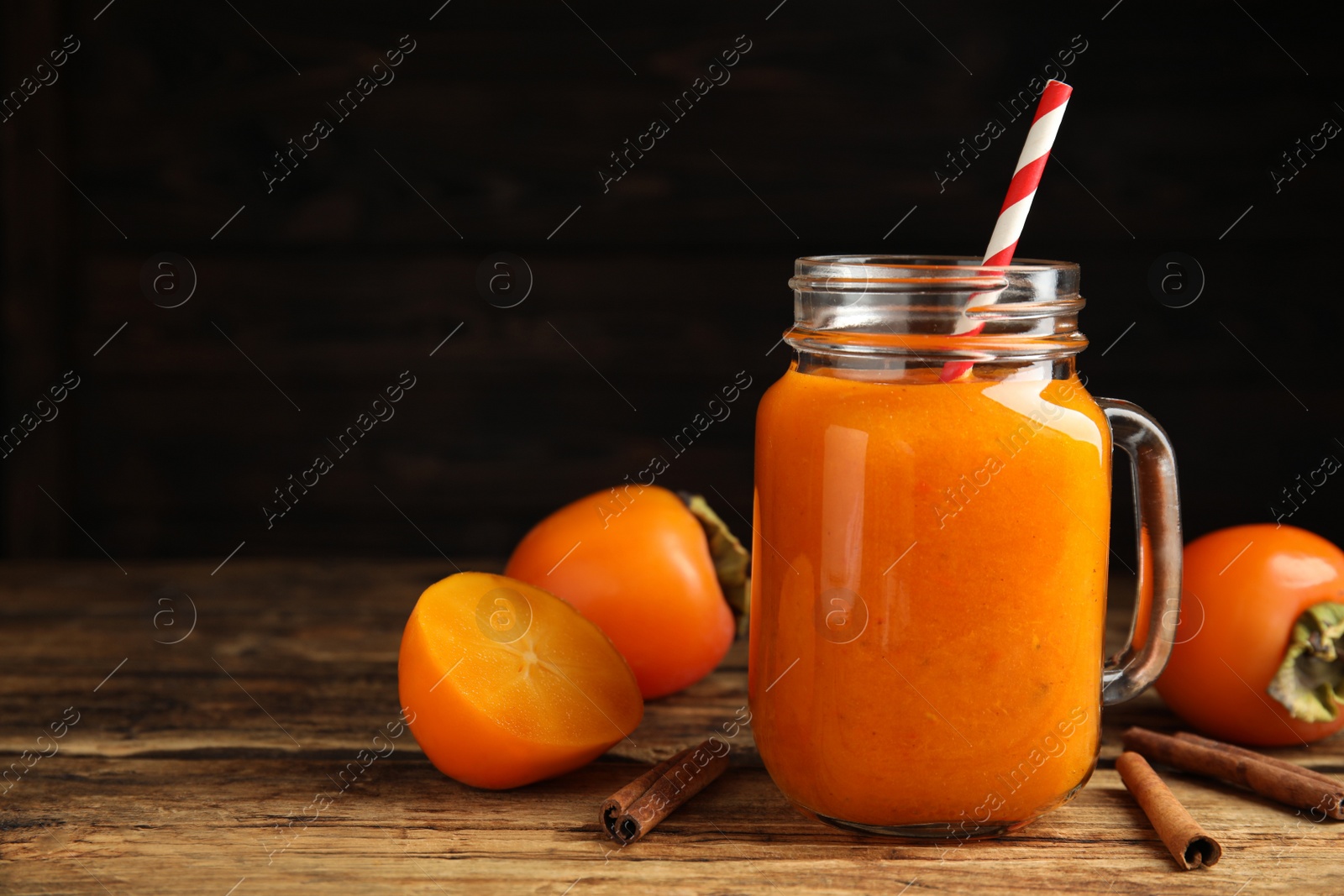 Photo of Tasty persimmon smoothie with cinnamon on wooden table against dark background. Space for text