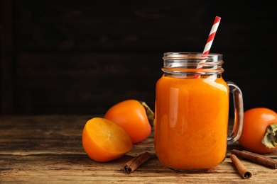 Photo of Tasty persimmon smoothie with cinnamon on wooden table against dark background. Space for text