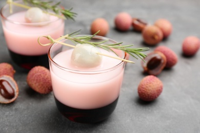 Photo of Lychee cocktail with fresh fruits and rosemary on grey table, closeup