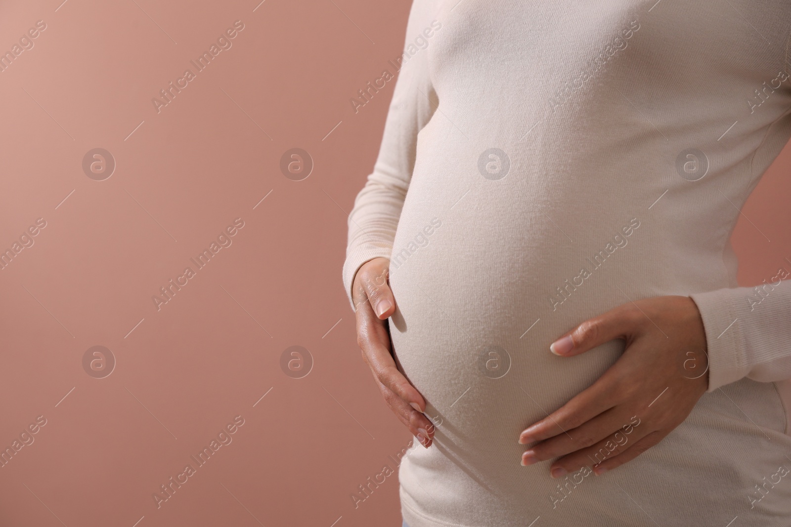 Photo of Pregnant young African-American woman on dusty rose background, closeup. Space for text