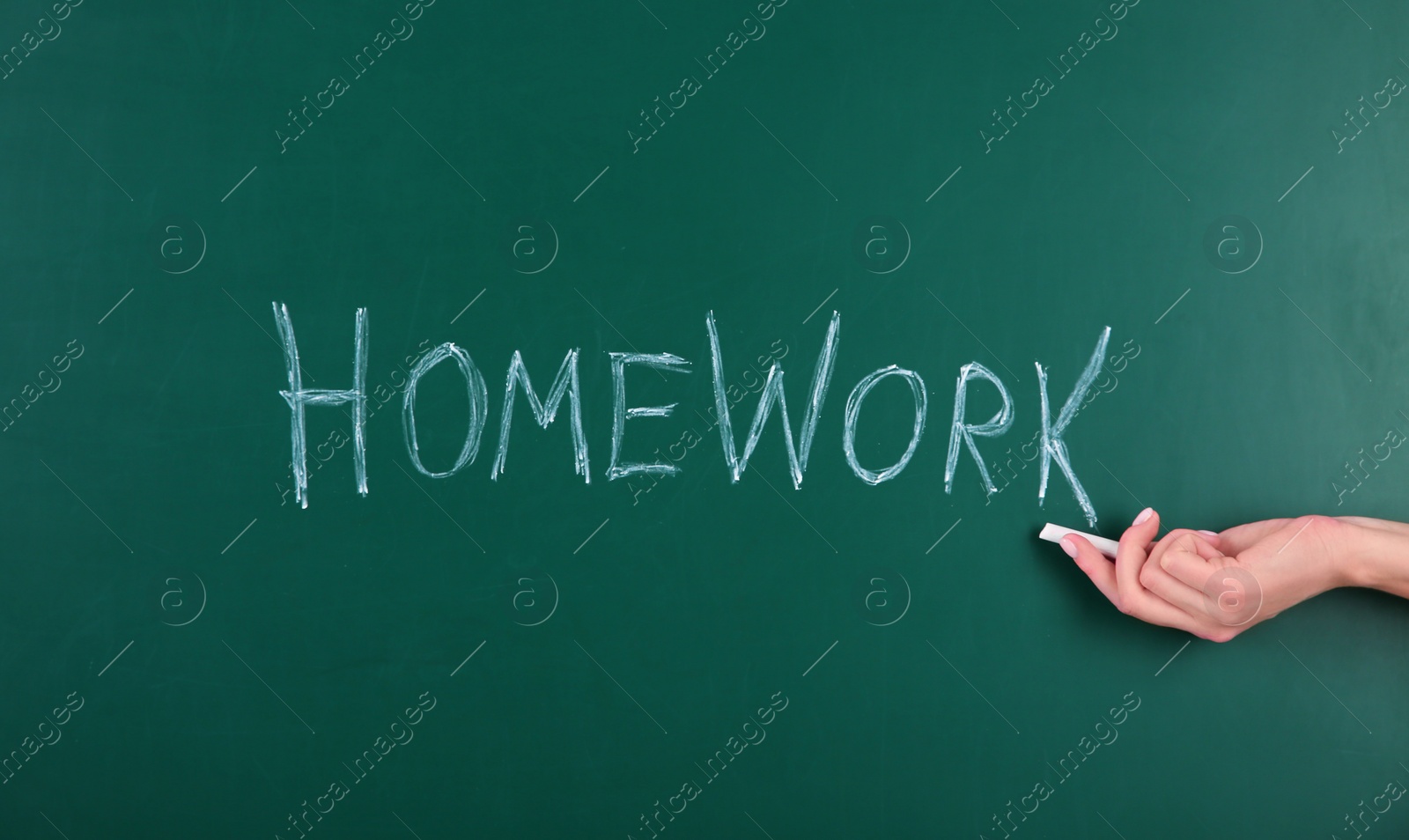 Photo of Woman writing word HOMEWORK on chalkboard, closeup