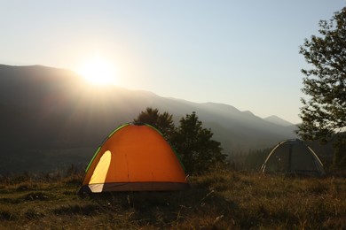 Photo of Two color camping tents on hill in mountains