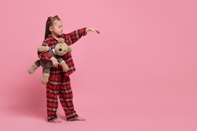 Photo of Girl in pajamas with toy bear sleepwalking on pink background, space for text