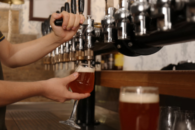 Photo of Bartender pouring fresh beer into glass in pub, closeup