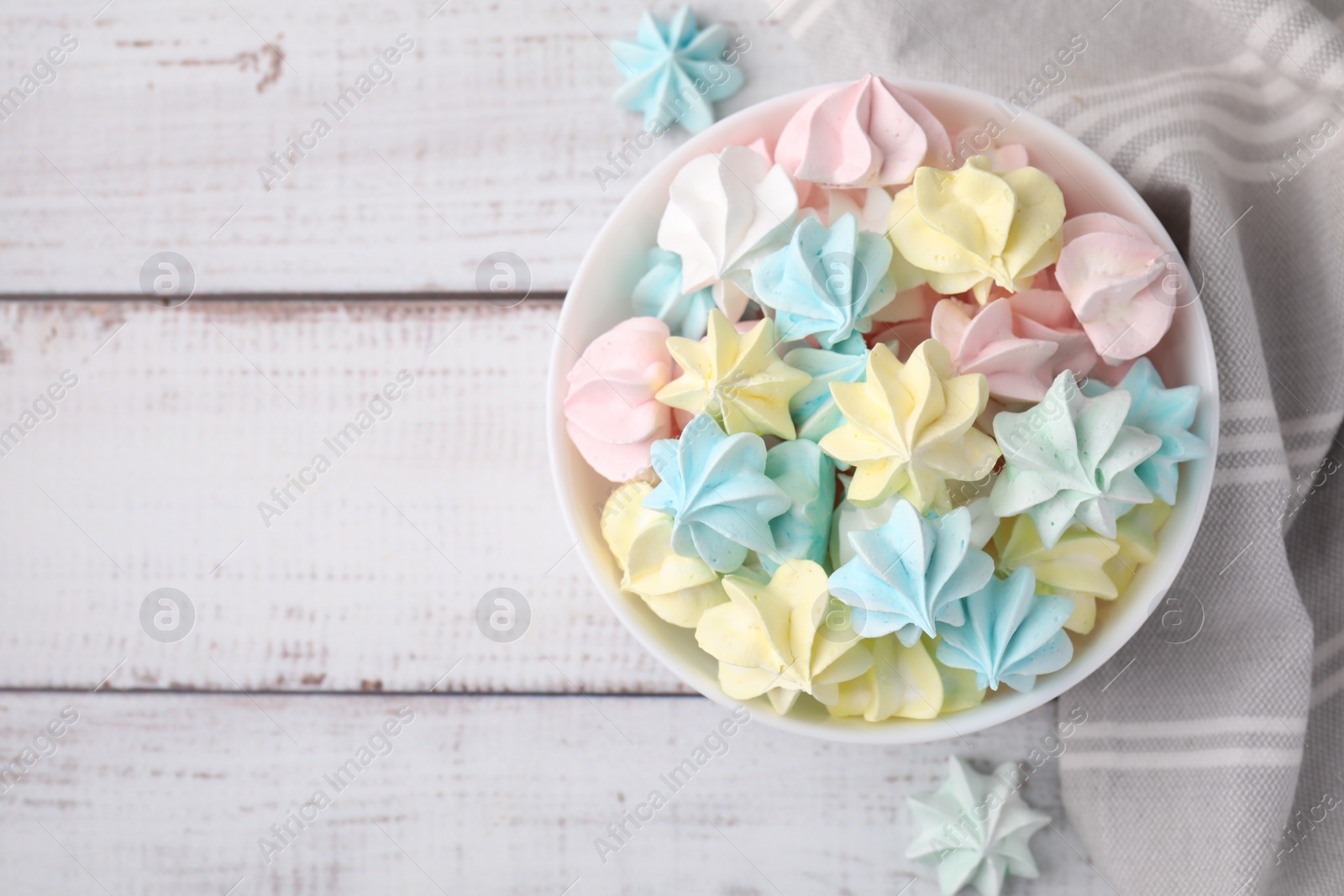 Photo of Tasty meringue cookies in bowl on white wooden table, top view. Space for text