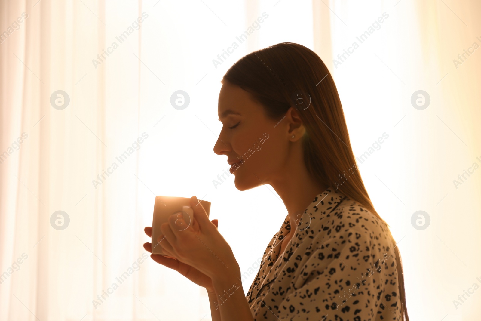 Photo of Young woman with drink near window at home. Lazy morning