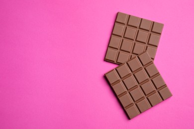 Pieces of tasty milk chocolate bar on pink background, flat lay. Space for text