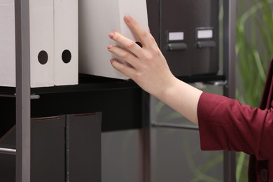 Woman taking folder with documents from shelf in office, closeup