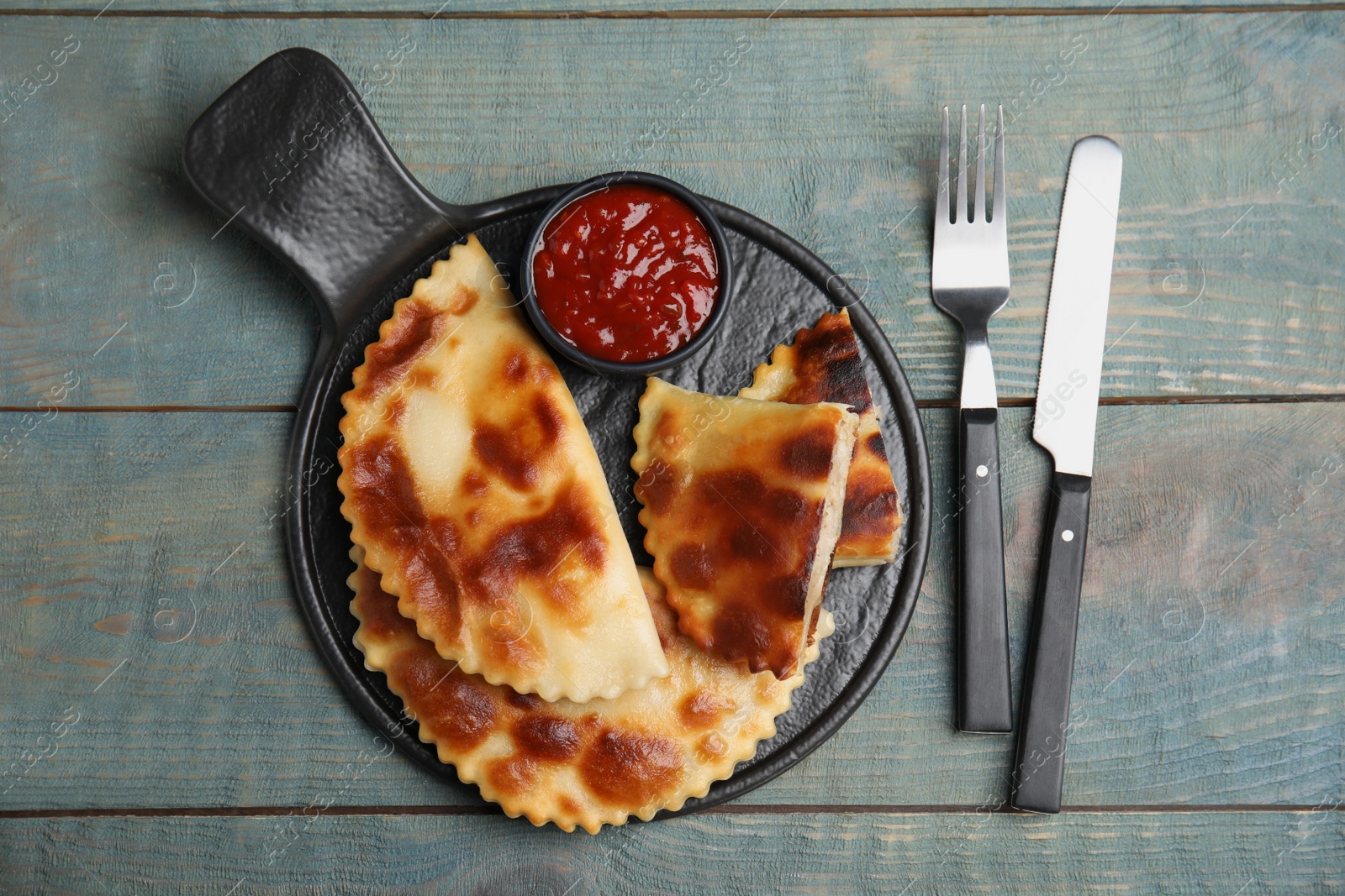 Photo of Delicious fried chebureki with ketchup served on light blue wooden table, flat lay