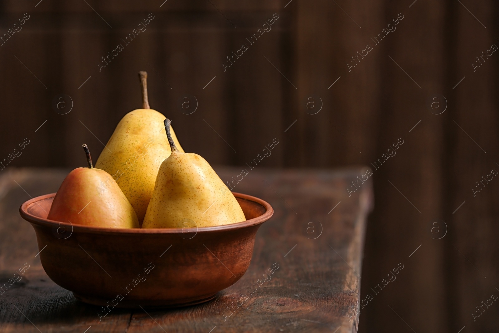 Photo of Bowl with ripe pears on wooden table. Space for text